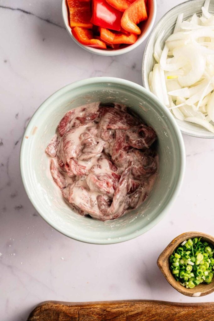 Sliced flank steak coated in a cornstarch and egg white marinade in a bowl.