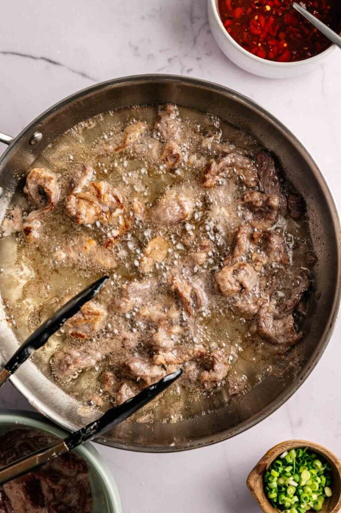 Crispy beef strips frying in hot oil in a stainless steel skillet.