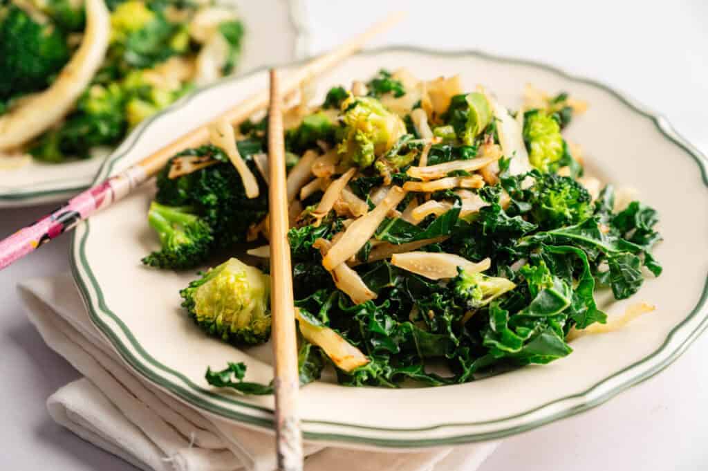 A plate of stir-fried vegetables, inspired by Panda Express Super Greens, features broccoli and leafy greens garnished with bamboo shoots, with chopsticks resting on the edge of the plate.
