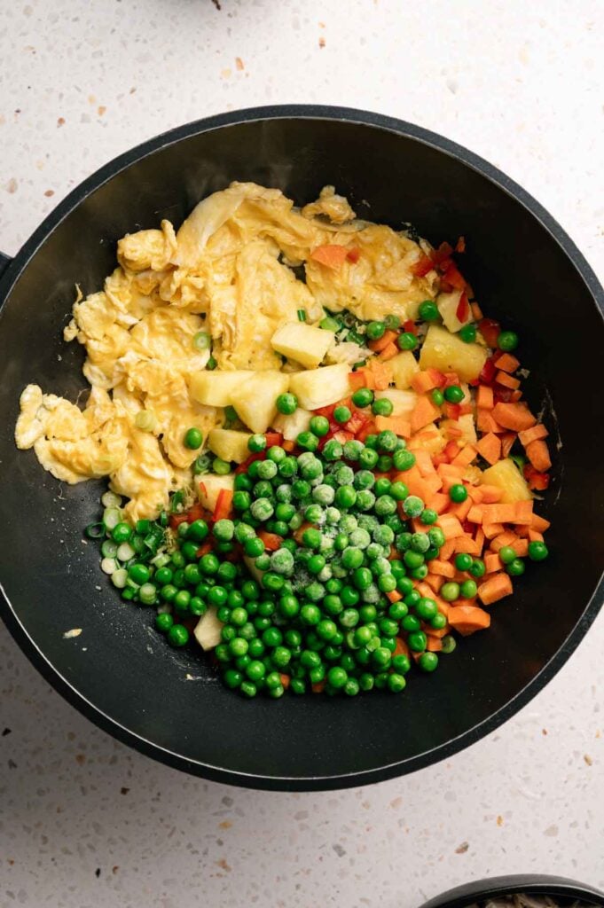 Diced pineapple, carrots, peas, and red bell pepper stir frying with scrambled eggs.