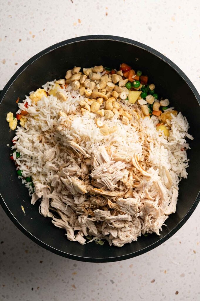 Shredded chicken, cashews, and rice added to a wok of stir-fried vegetables.