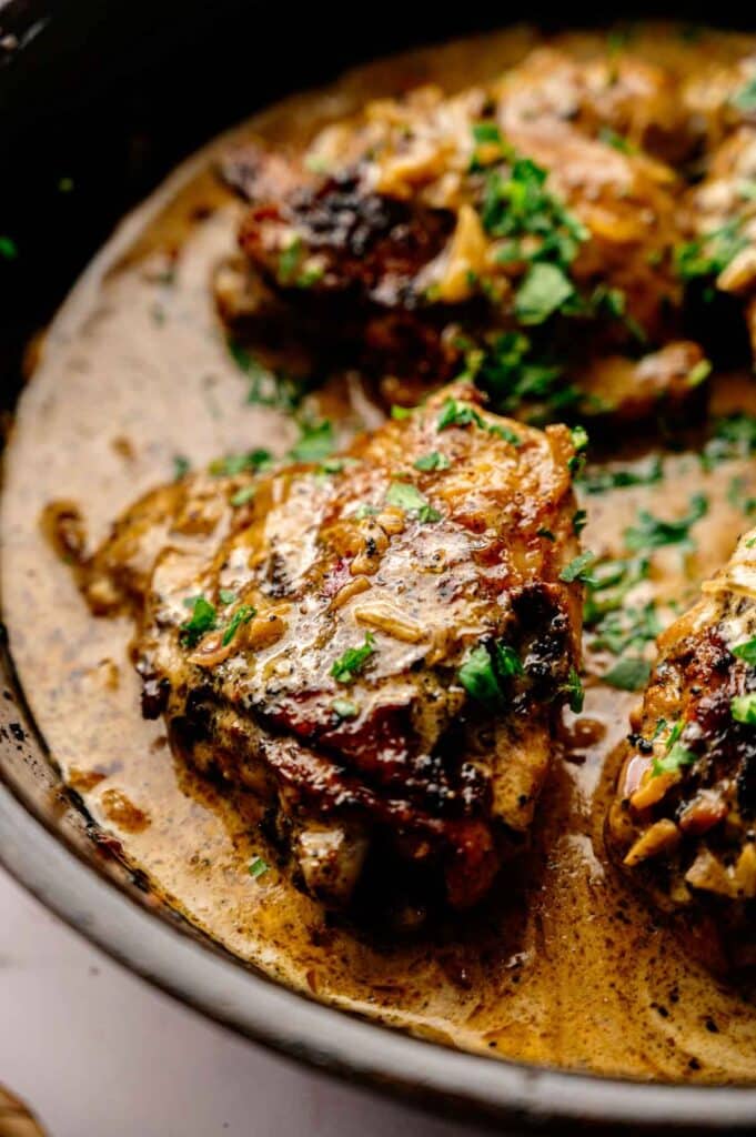 Creamy Skillet Chicken Thighs pan-seared and simmered in a rich, herb-infused sauce, then garnished with fresh chopped parsley and served hot in a skillet.