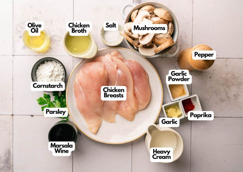 Top-down view of labeled ingredients for Slow Cooker Chicken Breast, including chicken breasts, mushrooms, olive oil, chicken broth, seasonings, parsley, cornstarch, garlic, and heavy cream.