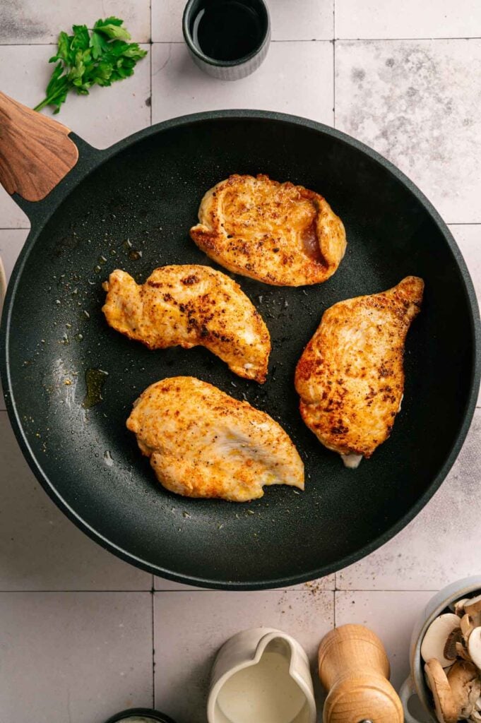Seasoned chicken breasts searing in a nonstick skillet until golden brown.