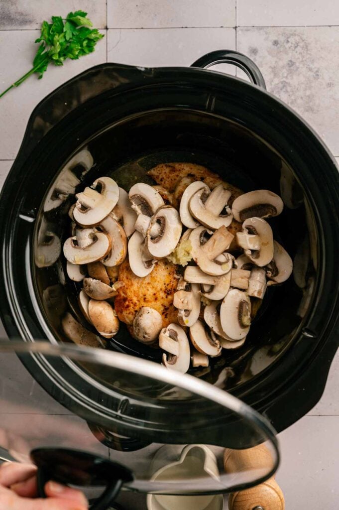 Seared chicken breasts topped with sliced mushrooms in a slow cooker.