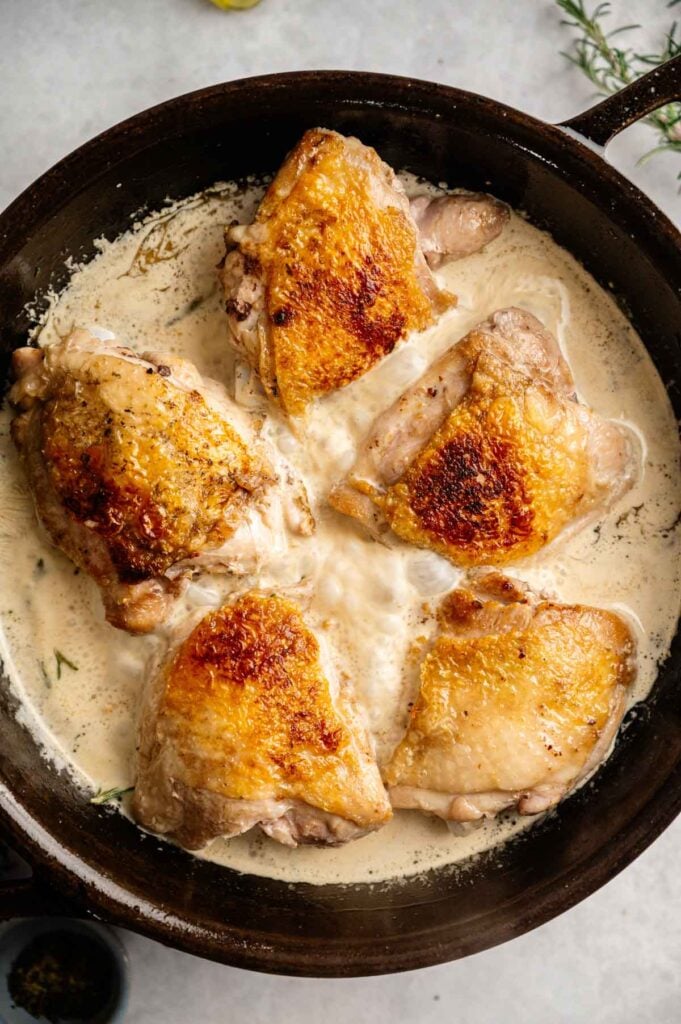 Seared chicken thighs nestled into a creamy Tuscan sauce in a cast iron skillet.