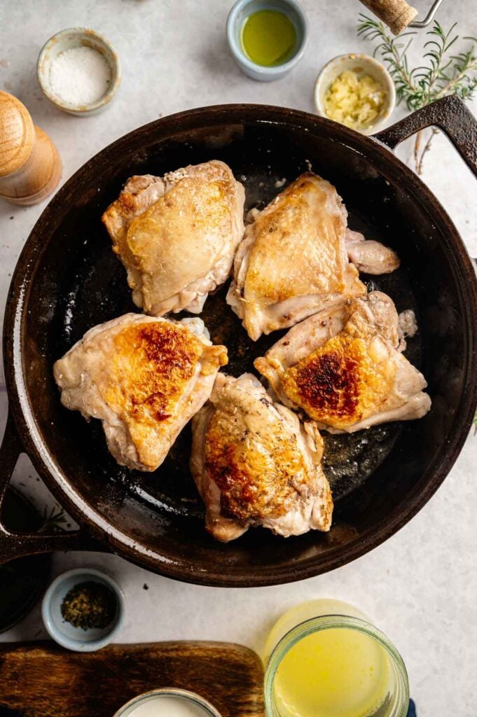 Chicken thighs searing skin-side down in a cast iron skillet until golden and crisp.