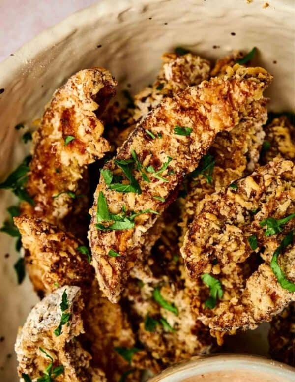 Close-up of breaded and baked mushroom slices garnished with chopped parsley in a ceramic bowl.