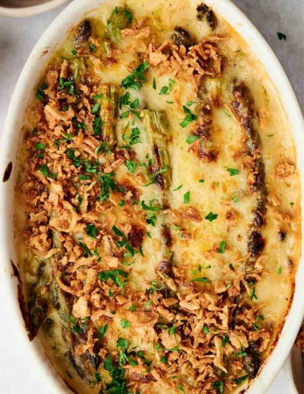 An oval baking dish filled with creamy asparagus casserole, topped with crispy fried onions and chopped parsley.