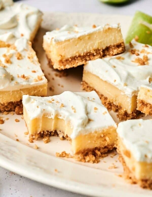 A plate of creamy dessert bars with a graham cracker crust and whipped topping, two with bites taken out.