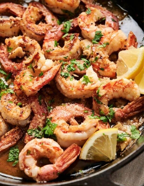 Cooked shrimp garnished with chopped herbs and served with lemon wedges in a skillet.
