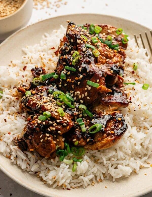 Grilled chicken glazed with sauce, garnished with sesame seeds and chopped green onions, served on a bed of white rice.