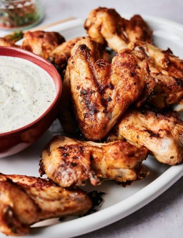A plate of grilled chicken wings served next to a bowl of creamy dipping sauce.