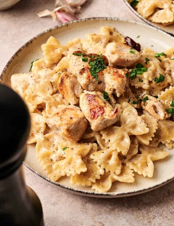 A plate of farfalle pasta topped with grilled chicken pieces and garnished with chopped parsley.