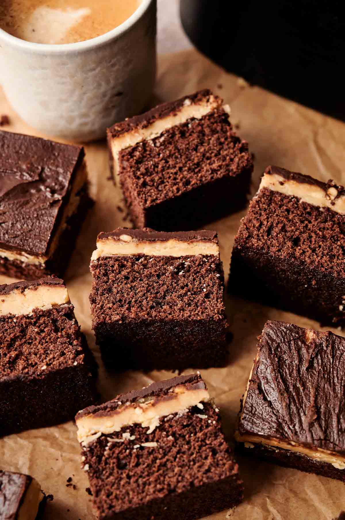 Slices of Air Fryer Buckeye Brownies with a creamy filling are arranged on parchment paper next to a cup of coffee.