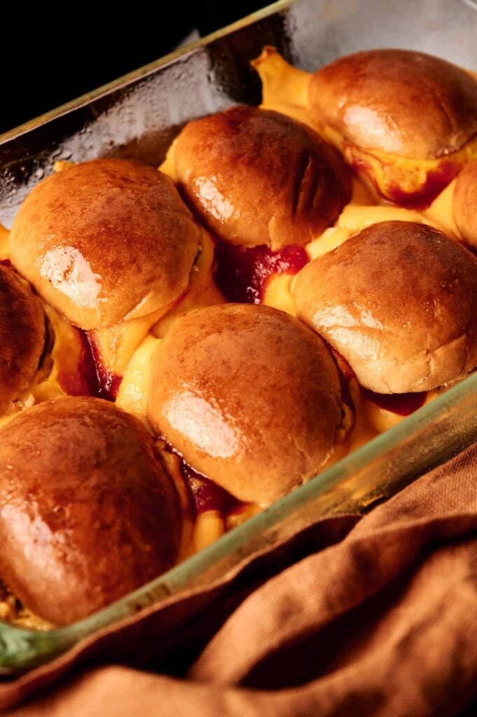A glass baking dish filled with baked Air Fryer Cheeseburger Sliders, topped with golden brown buns and melted cheese, sits next to a brown cloth.