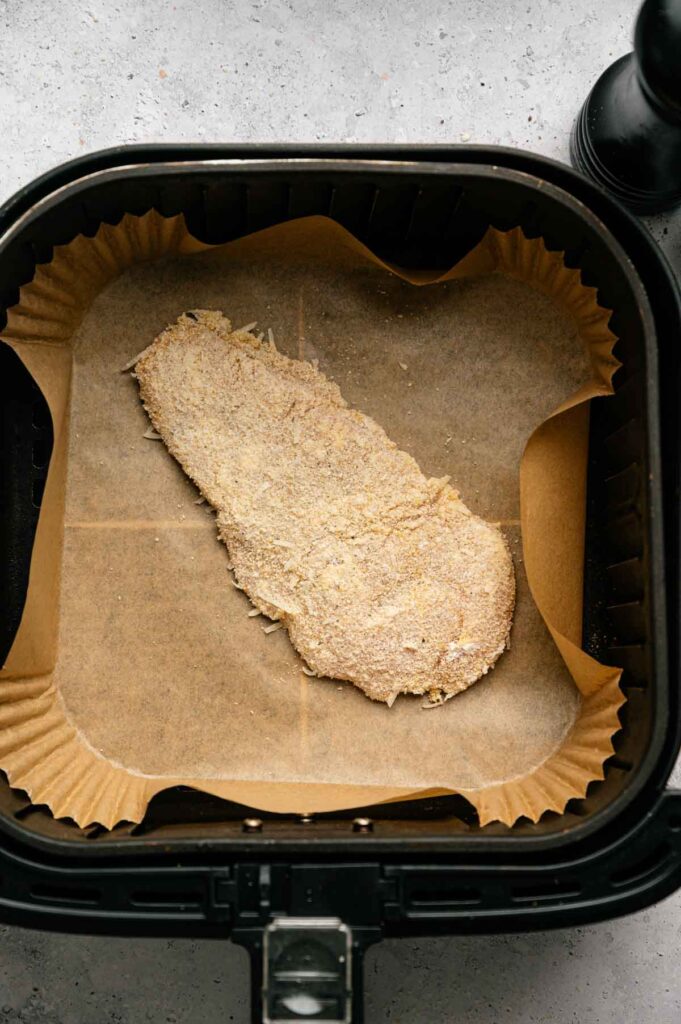 Air Fryer Chicken Cutlets: Breaded raw chicken placed on parchment paper inside an air fryer basket, ready to be cooked to crispy perfection.