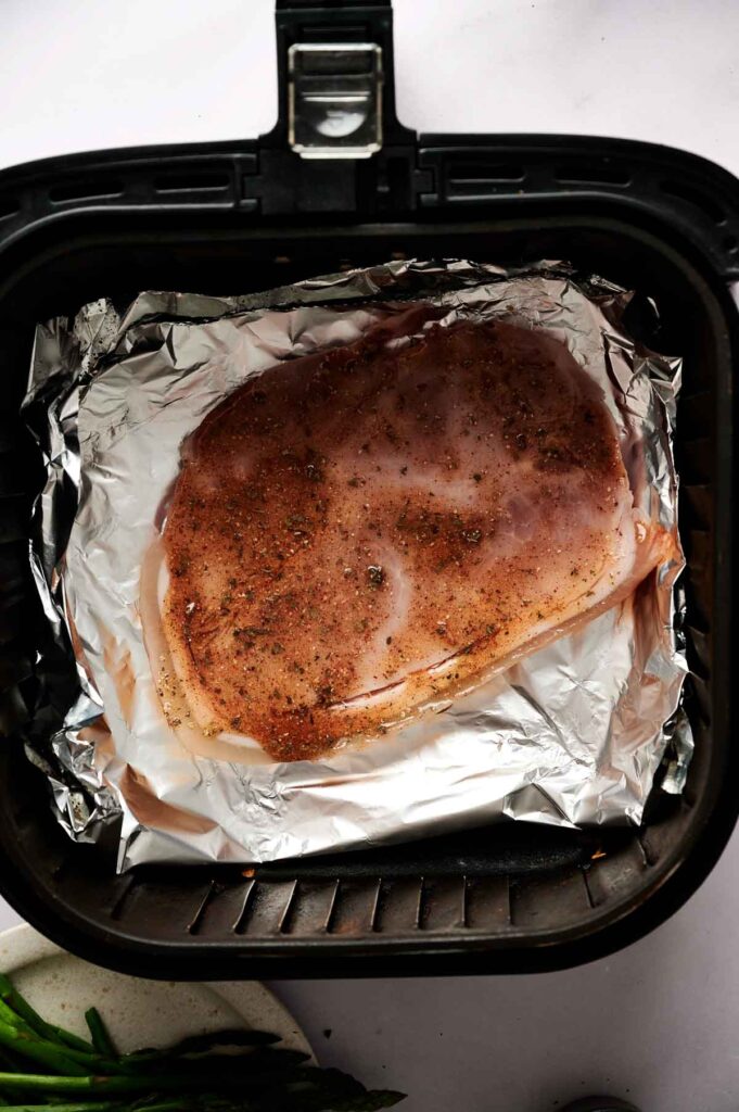 Raw seasoned chicken breast on foil inside an air fryer basket, ready to be cooked—just like preparing Air Fryer Ham Steaks for a quick and delicious meal.