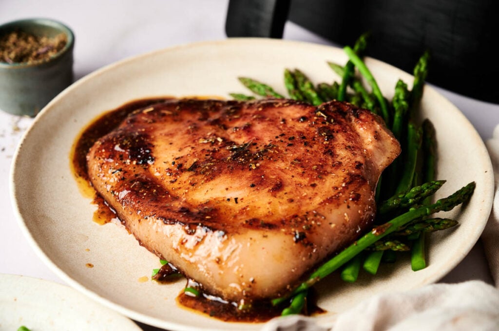 A cooked swordfish steak with sauce is served on a plate alongside steamed asparagus, offering a fresh alternative to classic dishes like Air Fryer Ham Steaks.