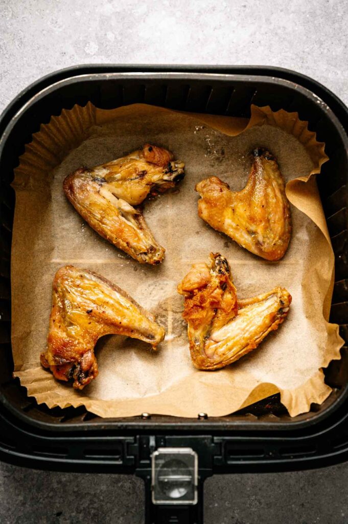 Four cooked Air Fryer Lemon Pepper Wings rest on parchment paper inside an air fryer basket.