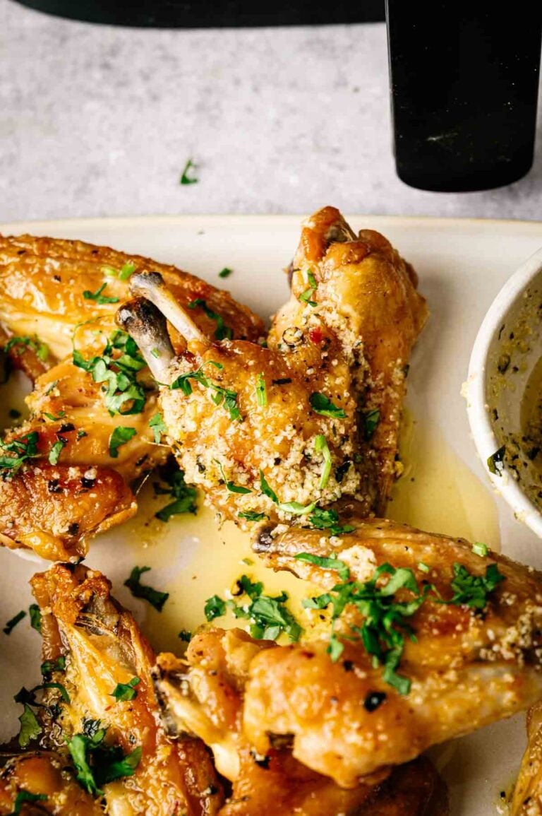 Close-up of Air Fryer Lemon Pepper Wings garnished with chopped parsley and grated cheese, served on a white plate with a side of dipping sauce.