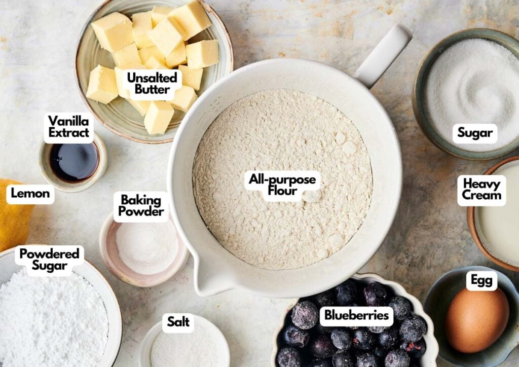 Baking ingredients for Air Fryer Blueberry Scones include all-purpose flour, cubed unsalted butter, sugar, heavy cream, egg, blueberries, salt, powdered sugar, baking powder, vanilla extract, and a lemon.