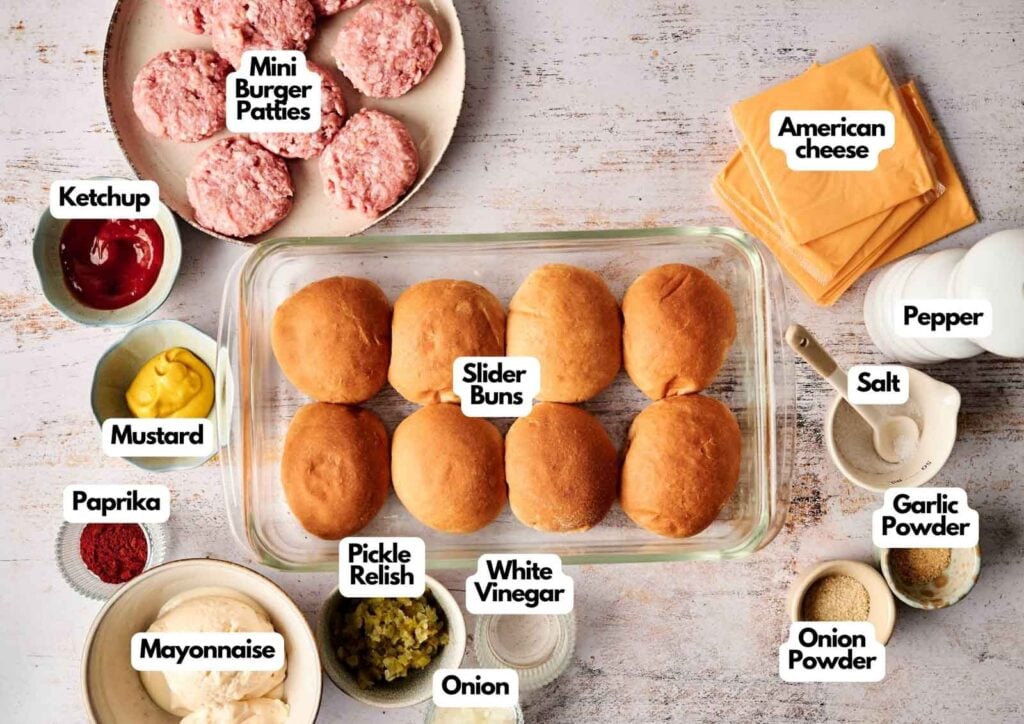 Ingredients for making Air Fryer Cheeseburger Sliders, including mini burger patties, slider buns, American cheese slices, condiments, spices, mayonnaise, onion, and pickle relish, arranged on a table.