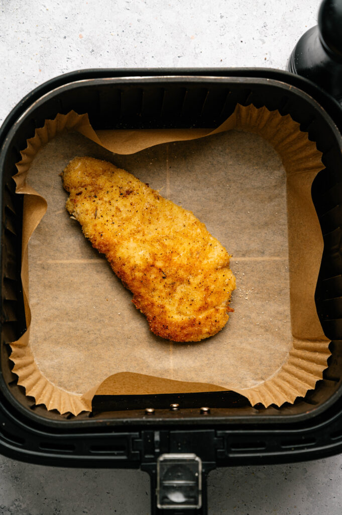 Crispy Air Fryer Chicken Cutlet rest on parchment paper inside the air fryer basket, ready to serve.
