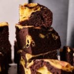 Stack of chocolate brownies with visible swirls of cheesecake, inspired by our Air Fryer Banana Pudding Brownies, displayed on a flat surface with a blurred background.