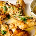 Close-up of Air Fryer Lemon Pepper Wings garnished with chopped herbs, served alongside a bowl of seasoned dipping sauce on a light-colored plate.