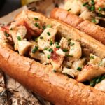 A close-up of an Air Fryer Lobster Roll in a toasted bun, filled with lobster meat, topped with chopped chives and black pepper, served on newspaper-style paper.