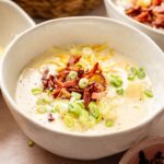 A bowl of creamy Loaded Baked Potato Soup topped with shredded cheese, bacon bits, and chopped green onions.