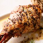 Slow Roast Leg of Lamb seasoned with herbs and spices, served on a white plate with savory juices pooling around the tender meat.