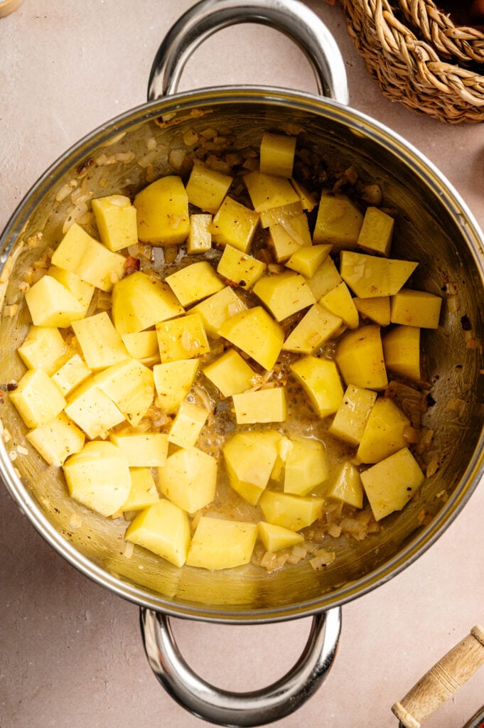 Diced potatoes cooking with onions in a stainless steel pot on a light-colored surface, perfect as the hearty base for Loaded Baked Potato Soup.