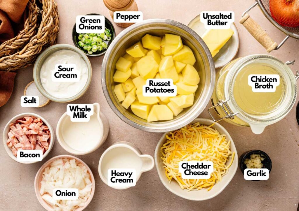 Various ingredients for Loaded Baked Potato Soup, including chopped russet potatoes, chicken broth, butter, cheddar cheese, green onions, sour cream, bacon, onion, garlic, salt, pepper, milk, and heavy cream.