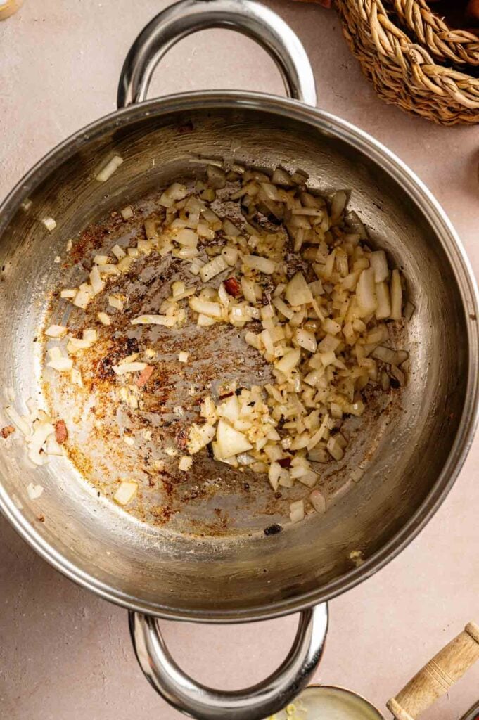 Chopped onions are being sautéed in a stainless steel pot, with some browning visible on the onions and the bottom of the pot—the perfect aromatic base for a hearty Loaded Baked Potato Soup.