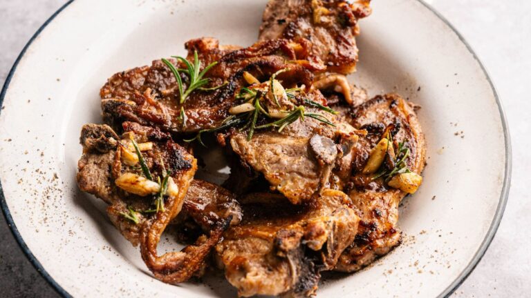 A plate of grilled lamb chops garnished with sprigs of rosemary and roasted garlic cloves.