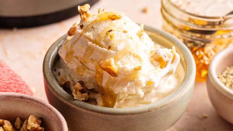 A bowl of vanilla ice cream topped with chopped nuts and drizzled with honey, with a jar of honey and a bowl of walnuts nearby.