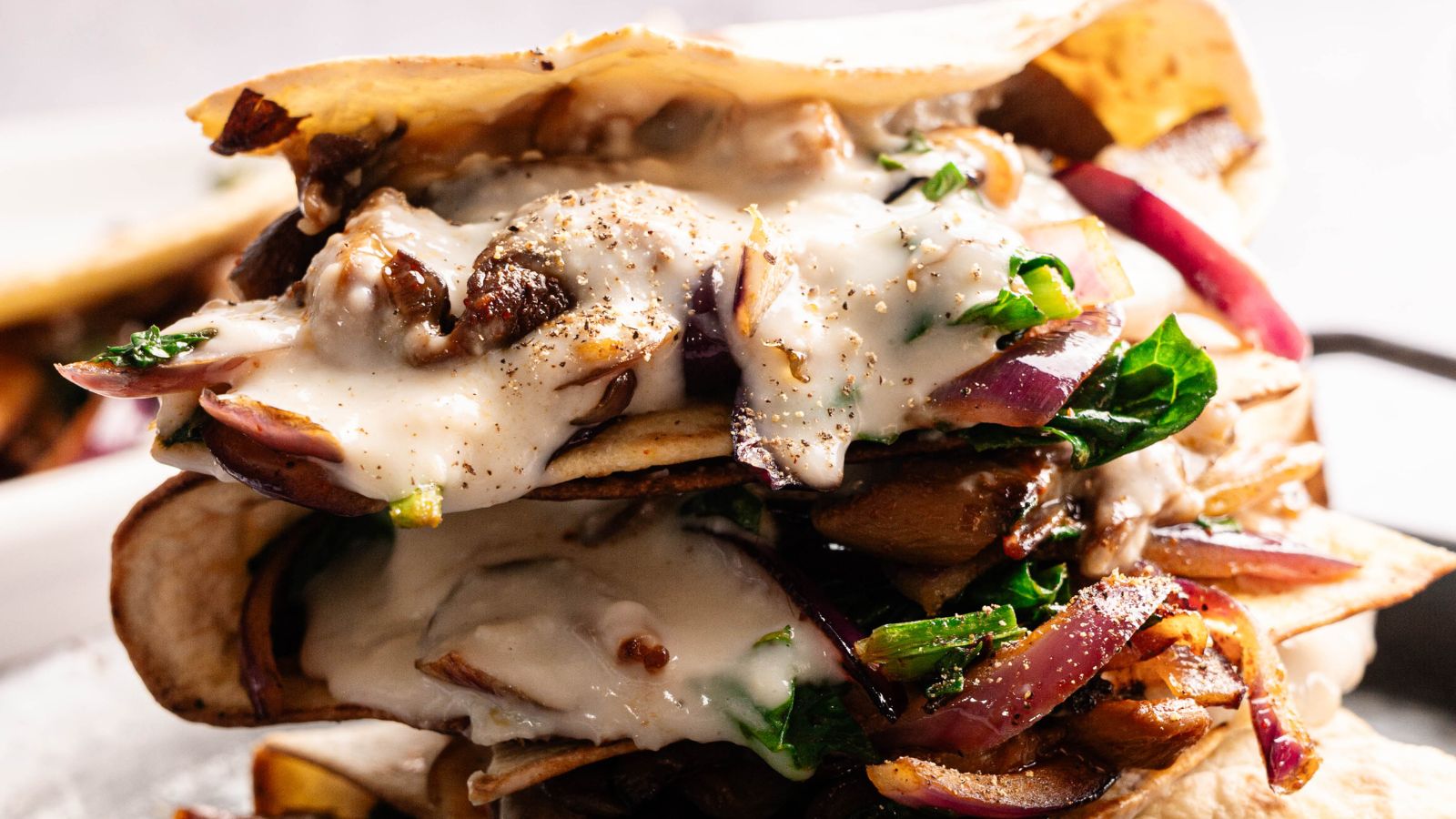 Stacked quesadillas filled with sauteed mushrooms, spinach, and red onions, topped with melted cheese sauce and black pepper.