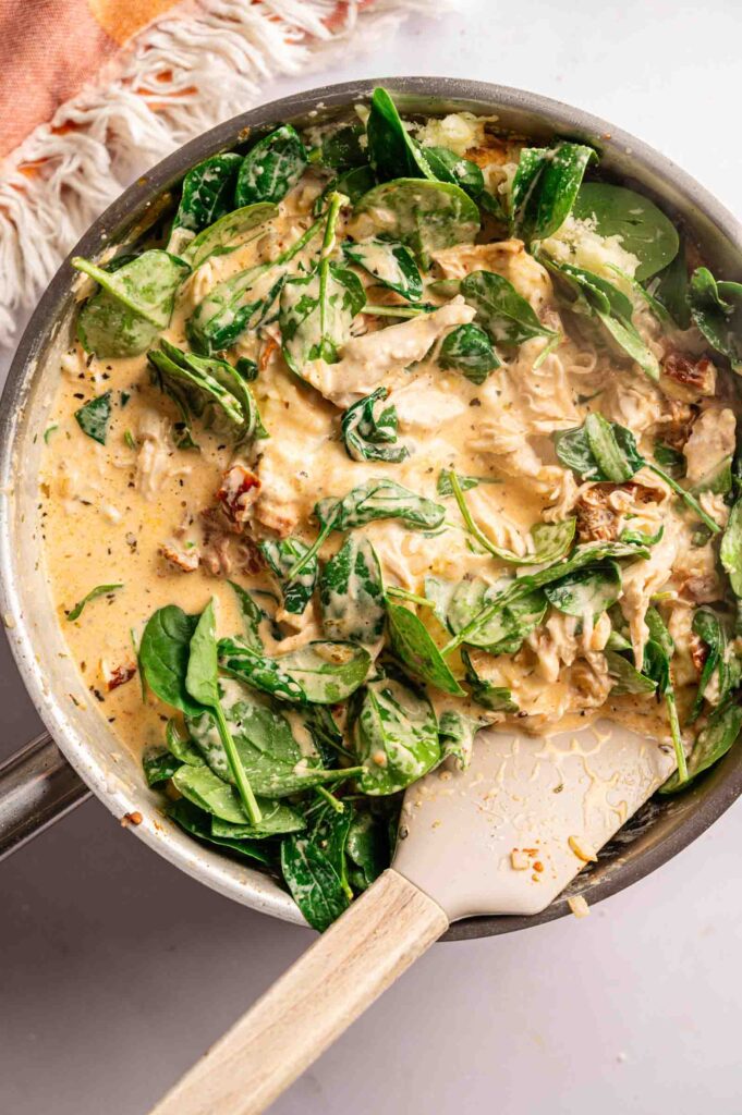 A skillet filled with creamy Marry Me Chicken pot pie filling — shredded chicken in a golden cream sauce with fresh baby spinach and sun-dried tomatoes.