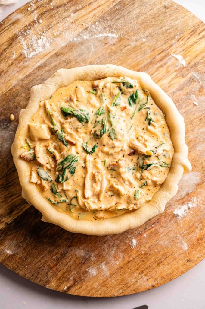 Unbaked Marry Me Chicken Pot Pie with creamy chicken and spinach filling in a crust, placed on a wooden surface.