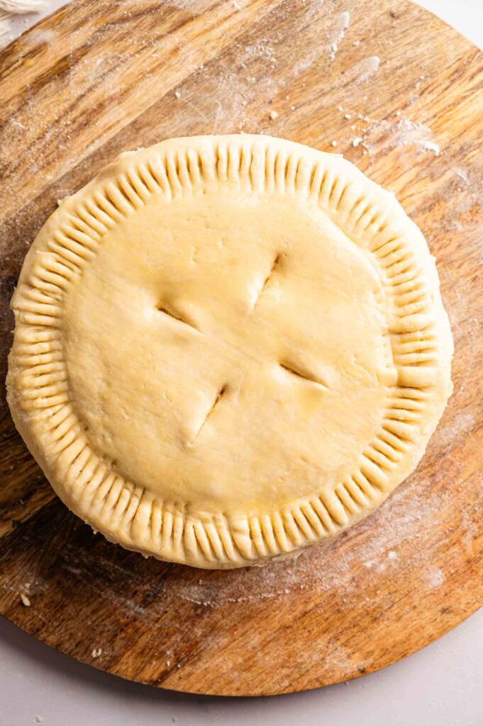 Unbaked Marry Me Chicken Pot Pie with a crimped edge and four slits in the top crust sits on a wooden surface.