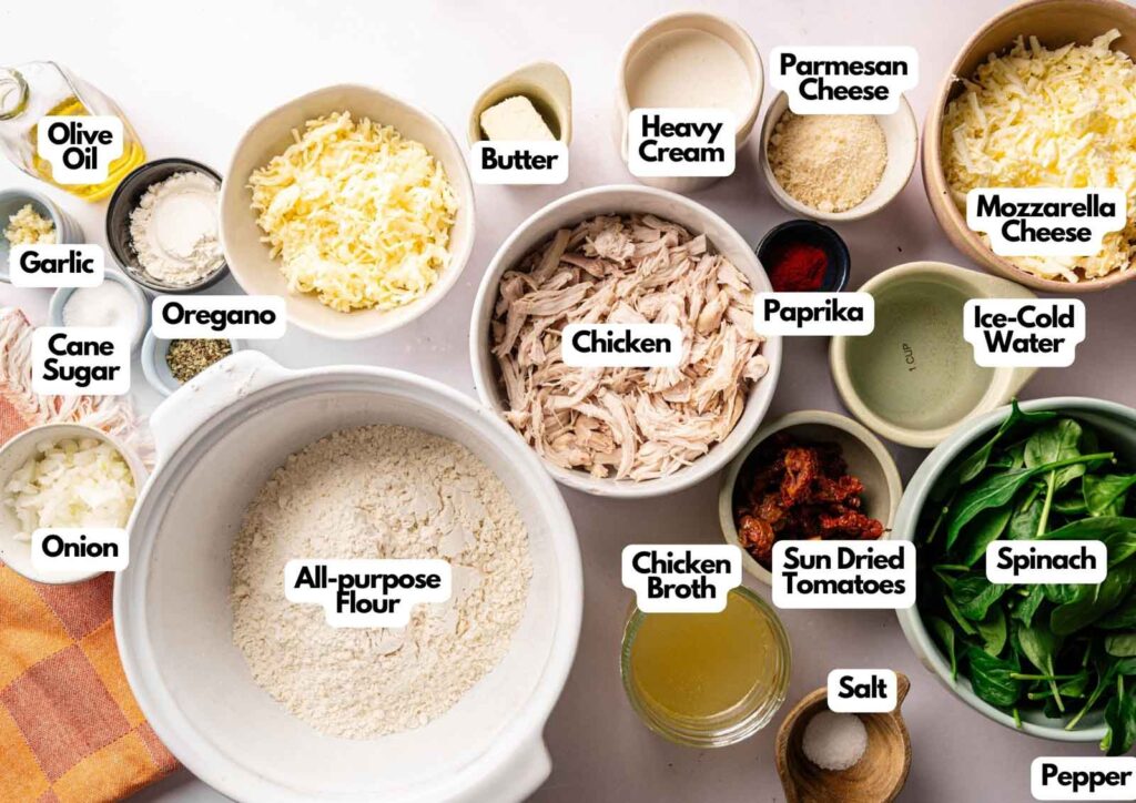 Top-down view of labeled ingredients for Marry Me Chicken Pot Pie—chicken, flour, cheeses, spices, vegetables, and liquids—arranged in bowls and dishes on a white surface.