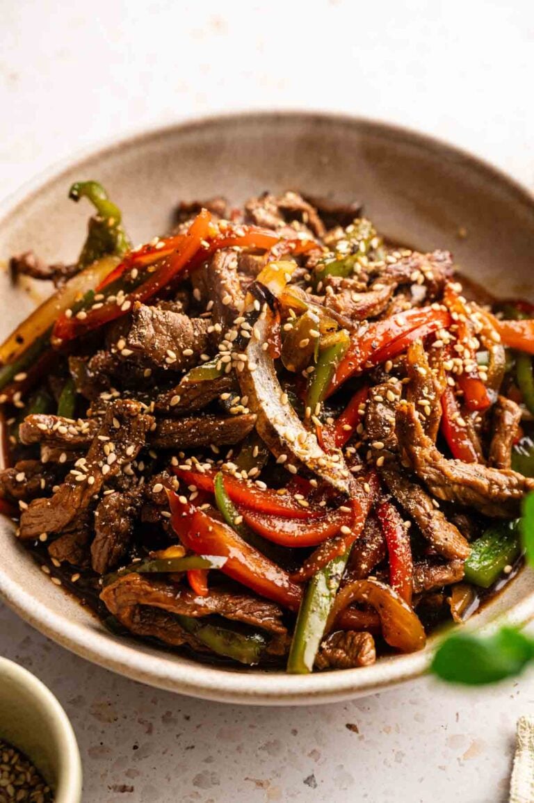 A bowl of stir-fried beef strips with red and green bell peppers, inspired by Panda Express Black Pepper Sirloin Steak, garnished with sesame seeds.