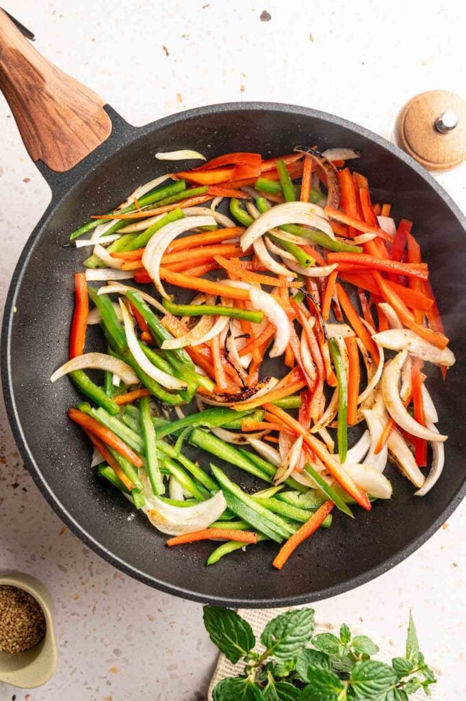 Colorful sliced vegetables cooking with charred edges for a beef stir fry.