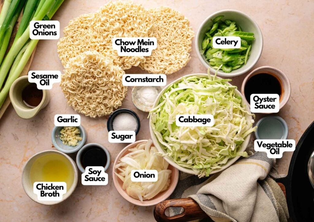 Chopped green onions, celery, cabbage, garlic, and onion, with chow mein noodles, cornstarch, sesame oil, soy sauce, sugar, chicken broth, oyster sauce&mdash;classic Panda Express Chow Mein ingredients on a countertop.