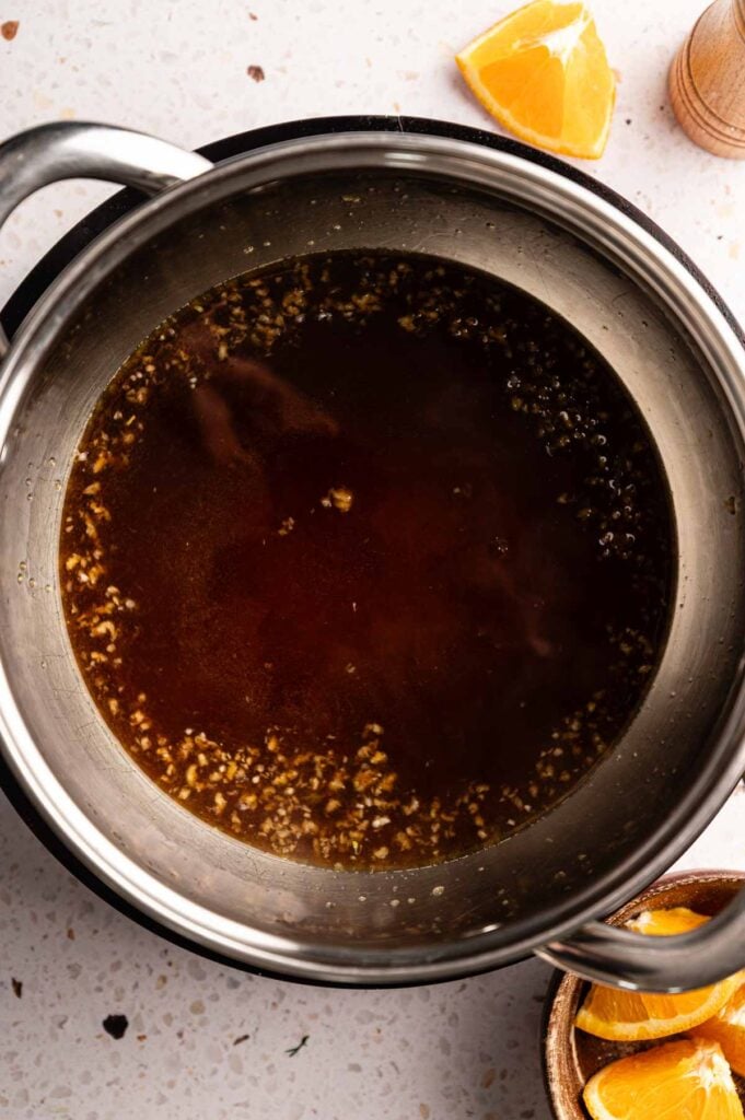 Glossy orange sauce with minced garlic simmering in a saucepan.