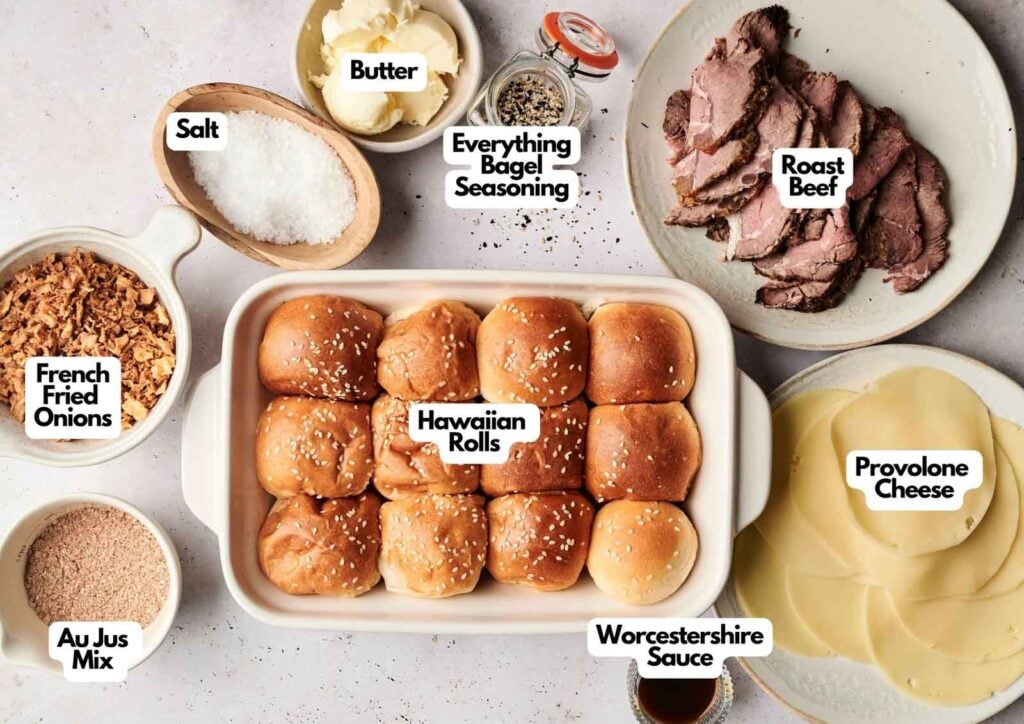 Ingredients for Air Fryer Roast Beef Sliders are arranged on a table, including Hawaiian rolls, roast beef, provolone cheese, butter, salt, Worcestershire sauce, au jus mix, French fried onions, and bagel seasoning.