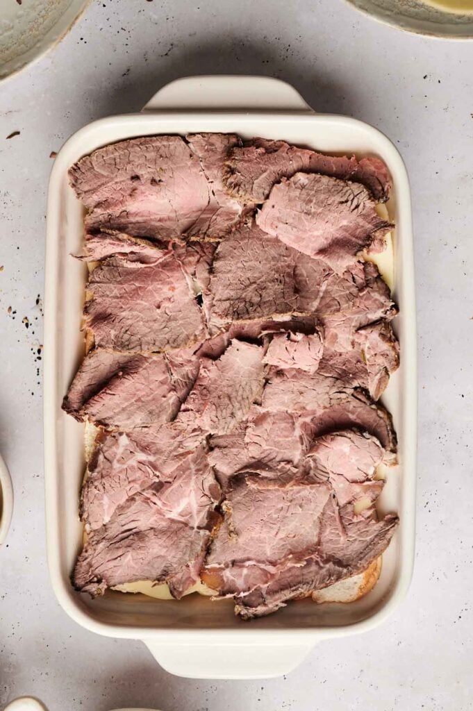 A white baking dish filled with overlapping slices of cooked roast beef, perfect for making Air Fryer Roast Beef Sliders, arranged neatly on top of a light-colored base.