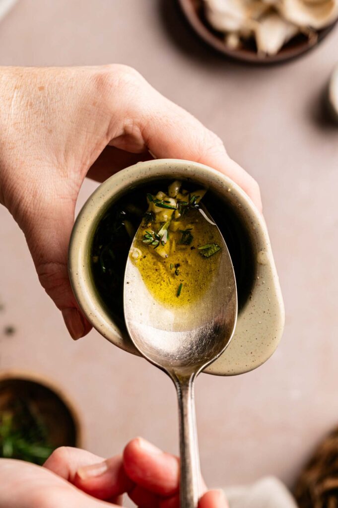 A spoon lifting a garlic and rosemary herb paste from a small bowl.